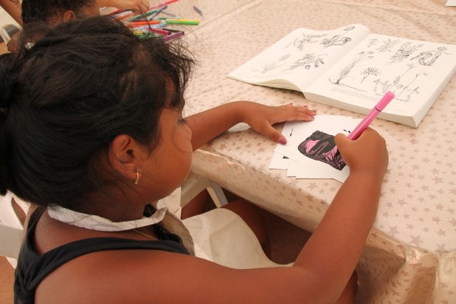 Une petite fille assise avec un feutre dans la main colorie une image